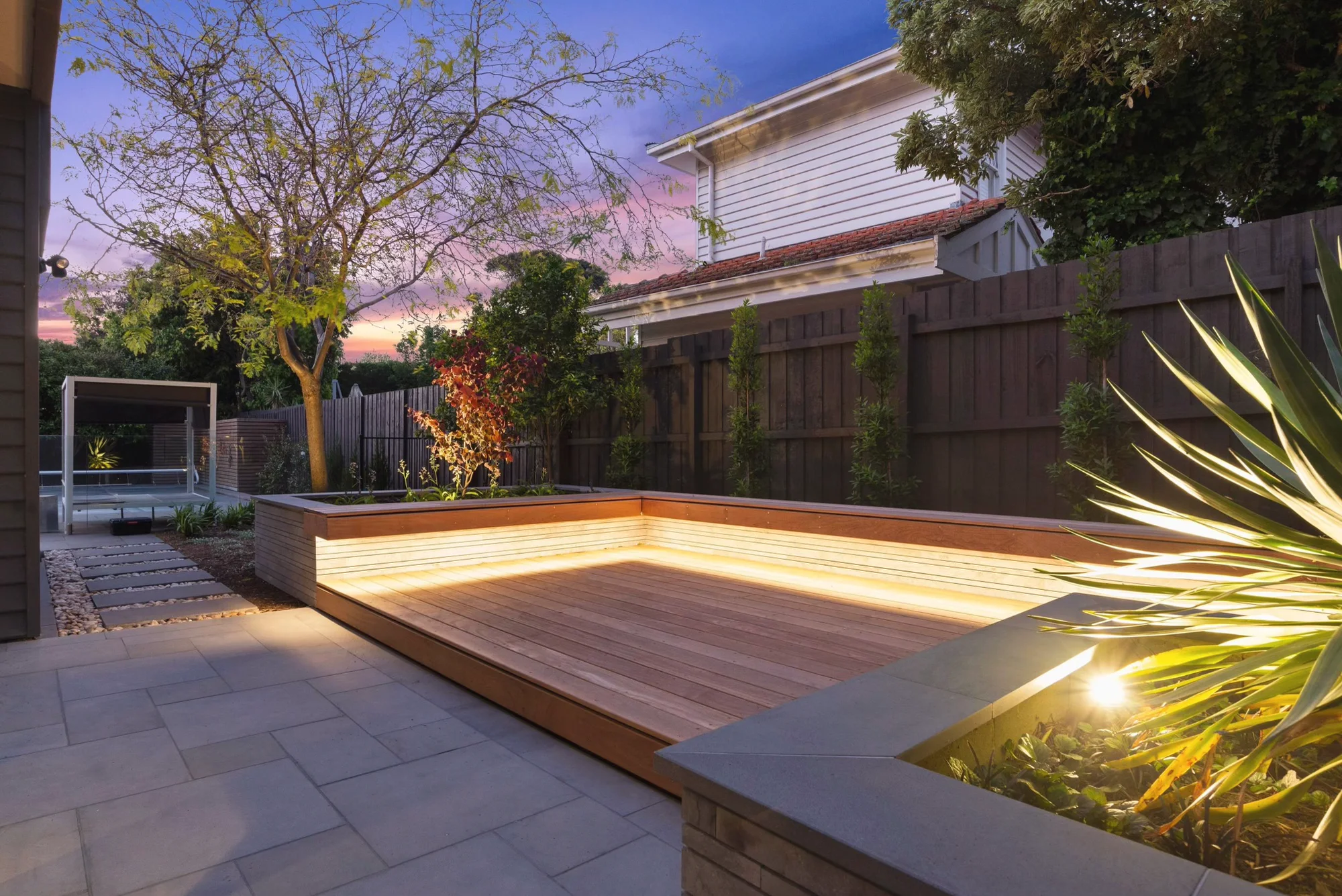 Hardwood deck with an LED strip, an uplit tree and a stone-clad planter at dusk