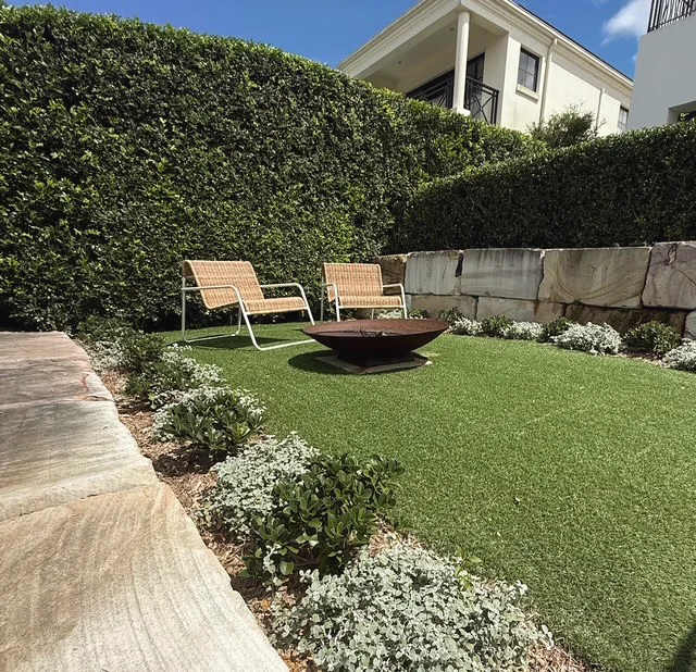 Sandstone block retaining wall and silver groundcover around a fire pit, sandstone paving in front