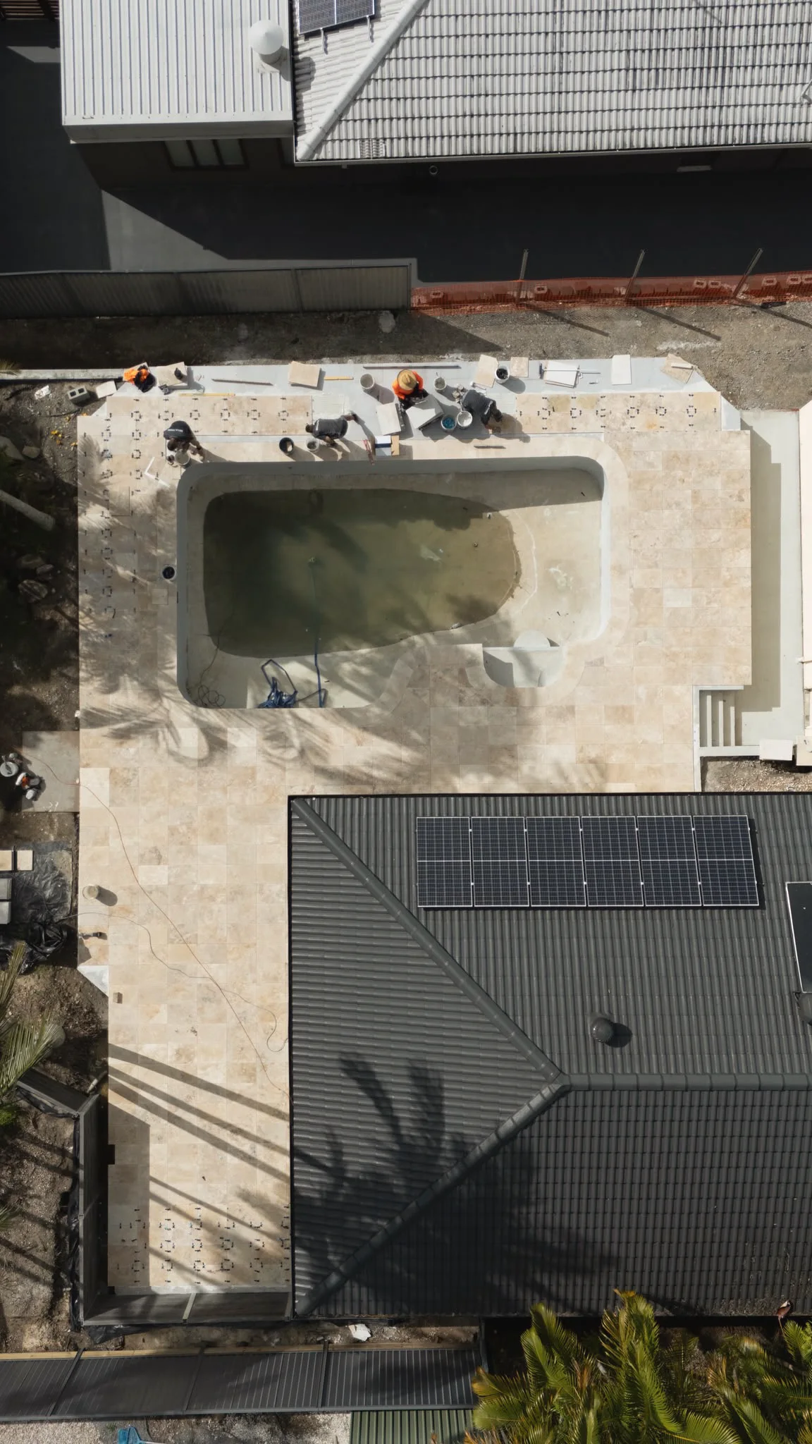 Drone view of the crew laying travertine around a pool mid-build