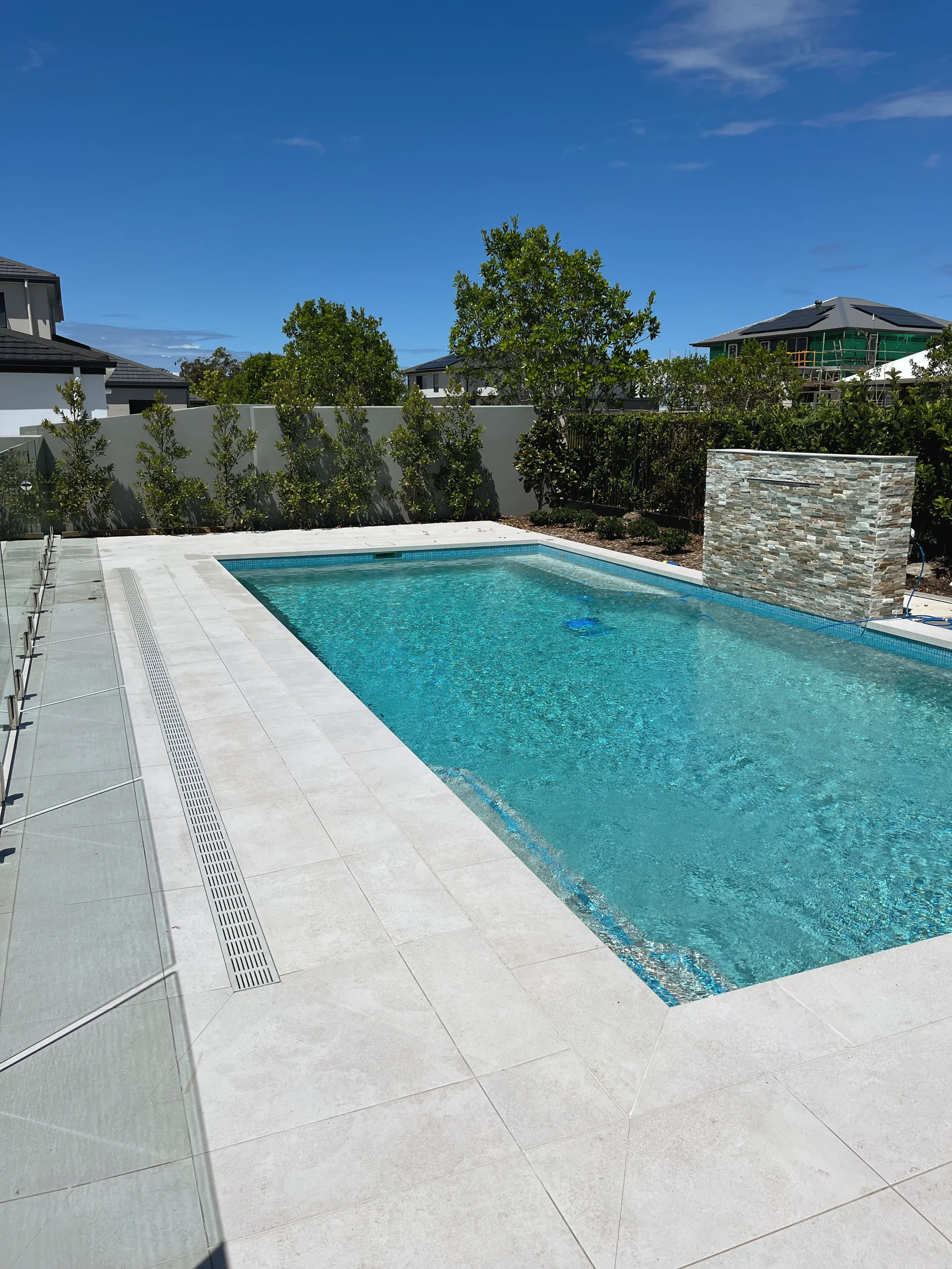 Rectangular pool with a pale paved surround, a stacked-stone water wall and a hedged boundary
