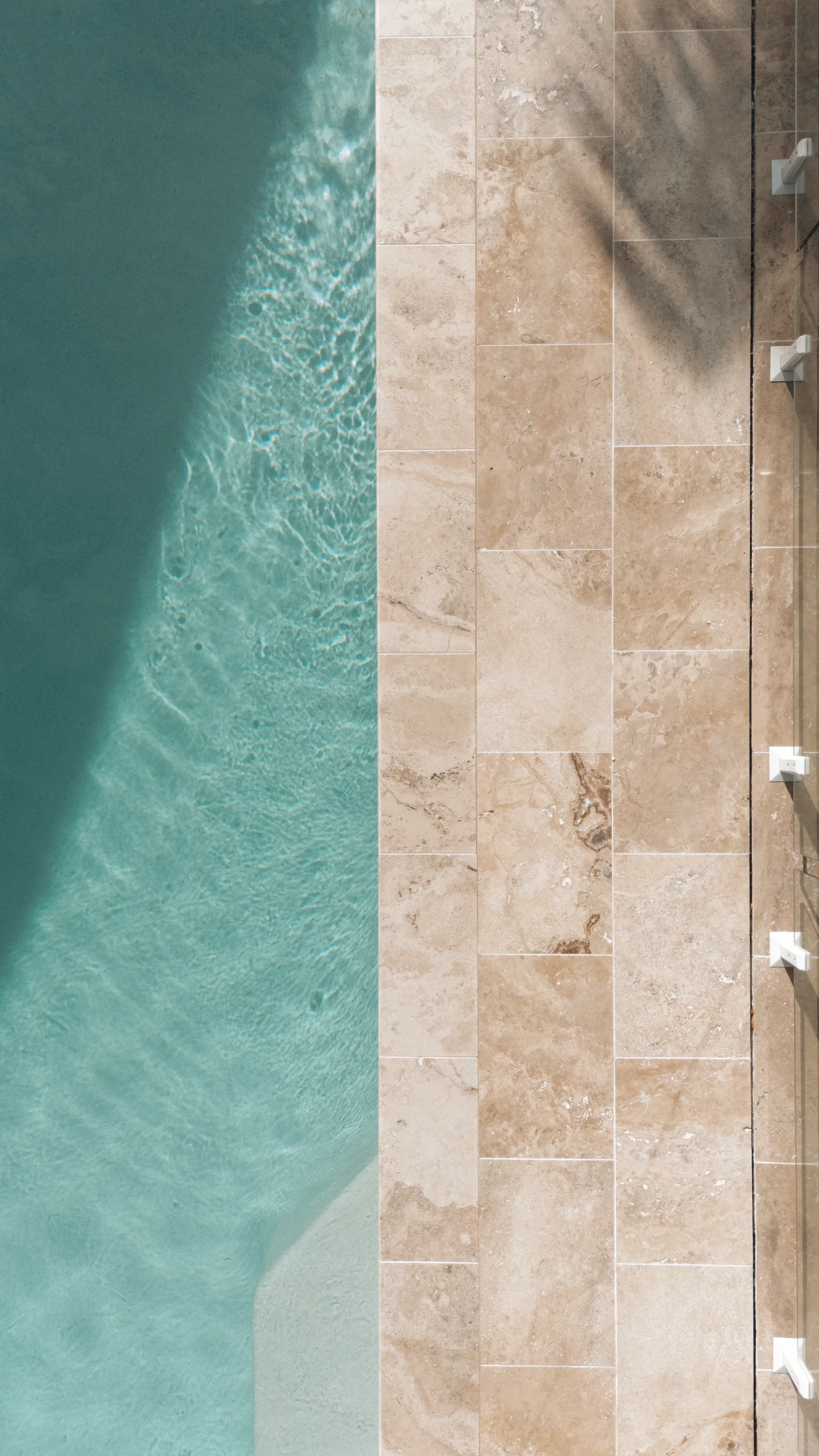 Looking straight down on travertine coping and paving along the edge of a pool