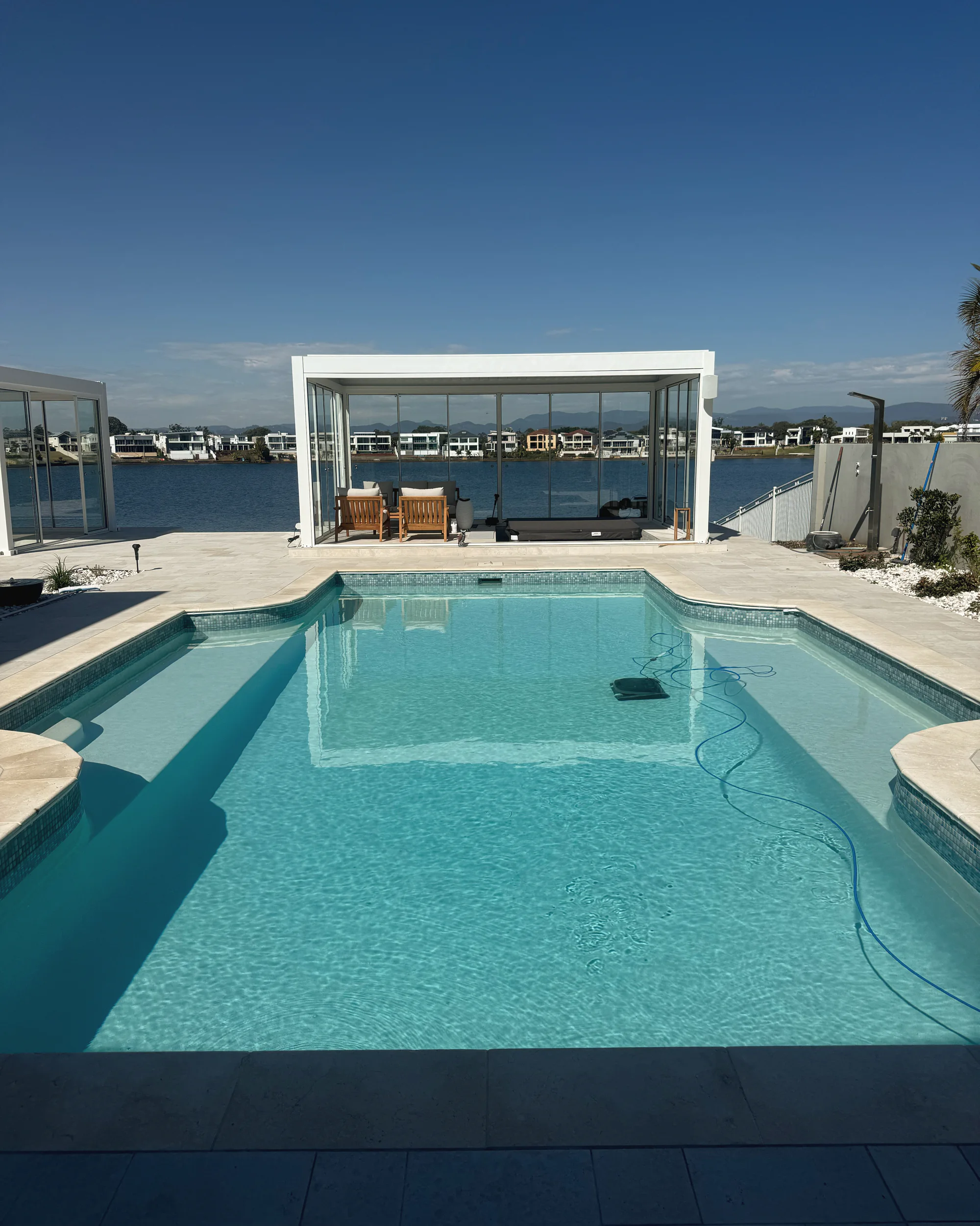 Pool with travertine coping on a waterfront block, a glass pavilion at the far end and the water beyond