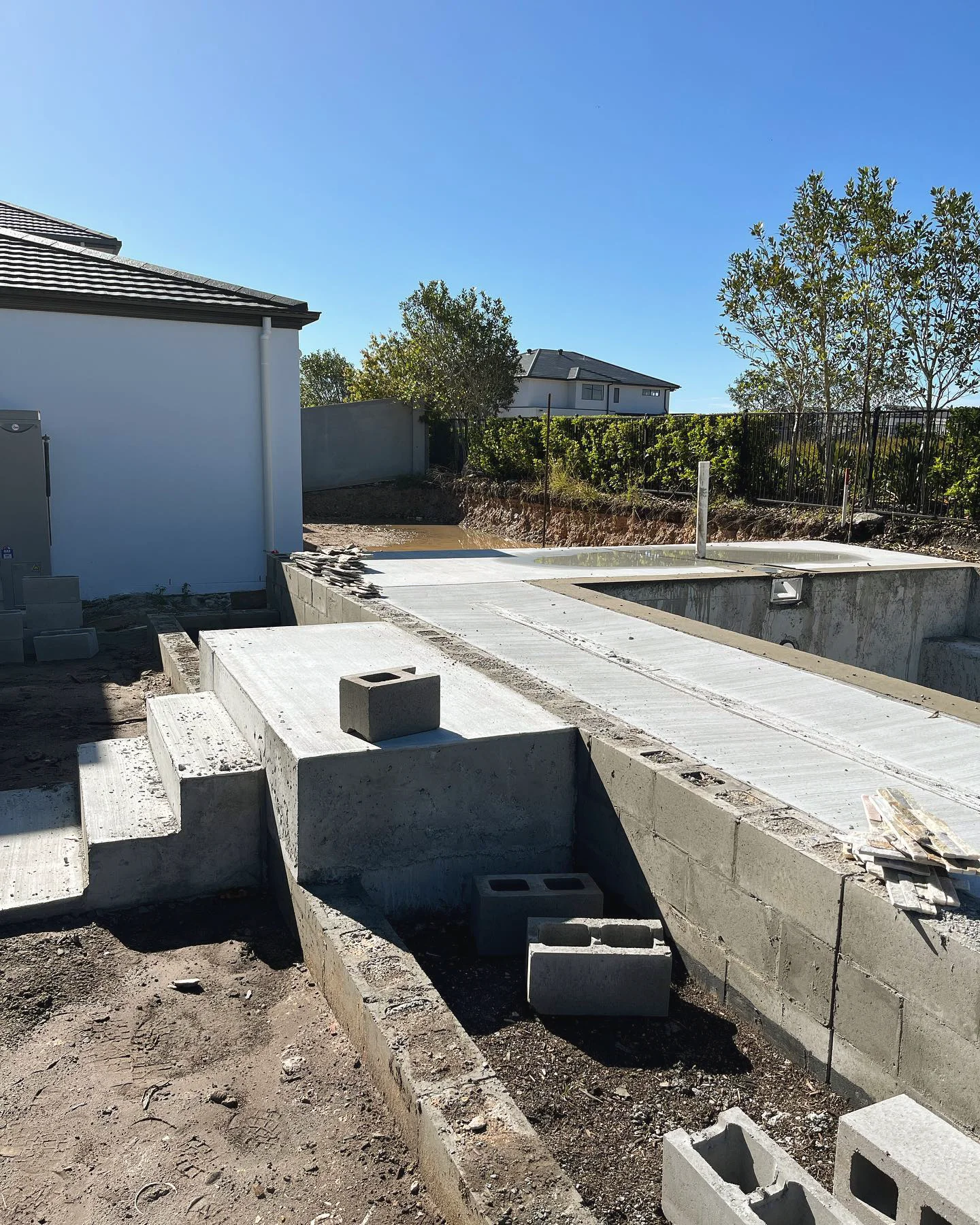 Core-filled block retaining walls and steps going up beside a new pool, mid-build