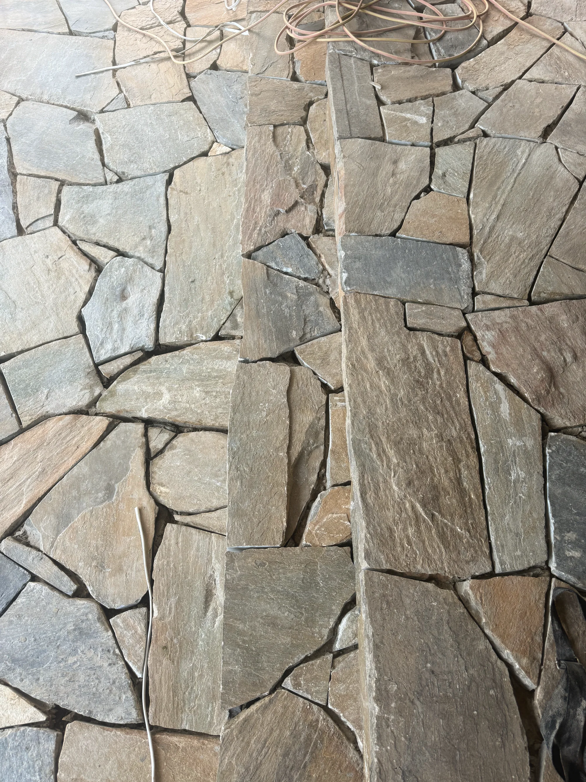 Natural stone being fitted to a pillar beside crazy paving, mid-build